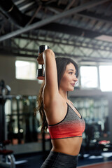 Fototapeta premium A slim sportswoman doing strength workout with dumbbells in a gym.