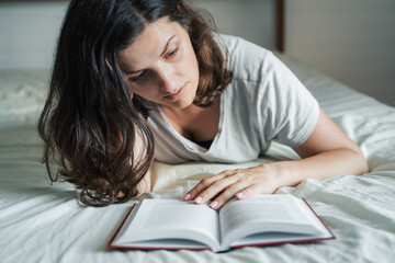 Woman lying on bed and reading a book. Relax at home. Distance education, learning