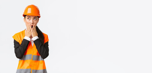 Shocked and concerned asian female engineer, architect in safety helmet and reflective jacket,...
