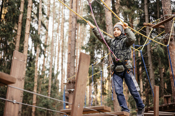 Teenager boy in safety equipment routing and climbing in adventure rope park. Child in helmet...