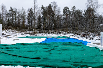 Foundations for a residential house in snowy winter scene. Blue and green covering.