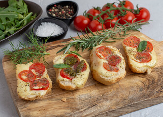 Italian bruschetta with roasted tomatoes, mozzarella cheese and herbs on a cutting board