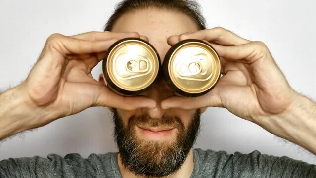 Close-up of a happy man putting two beer cans to his eyes as if they were binoculars