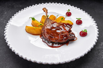 Duck leg with pear in caramel, on a white plate