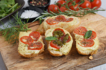 Italian bruschetta with roasted tomatoes, mozzarella cheese and herbs on a cutting board