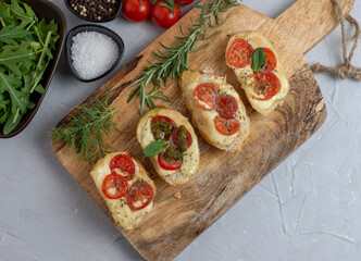 Italian bruschetta with roasted tomatoes, mozzarella cheese and herbs on a cutting board