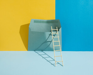 A surreal minimalist composition made of a wooden ladder and an envelope on a blue, pastel blue and...