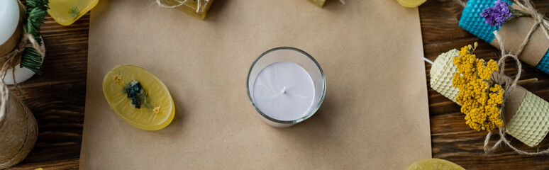 Top view of candle in glass near soap on craft paper on wooden surface, banner.