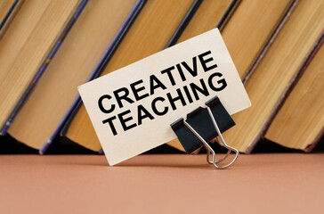 On the table against the background of books is a business card with the inscription - Creative Teaching