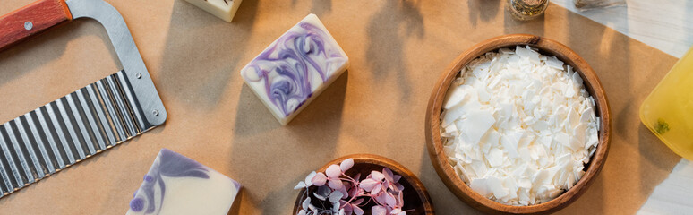 Top view of handmade soap bars near flakes and flowers on craft paper, banner.