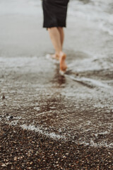 legs of a young woman walking by the sea, images of legs, black dress, seashore, waves