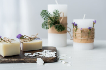 Fototapeta na wymiar Craft soap on cutting board near blurred candles on table.