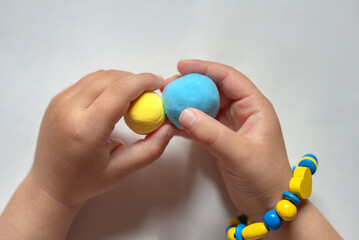 Child with plasticine in the colors of the flag of Ukraine in hands. Ukrainian flag do it yourself. A child make the flag of dough. Children's creativity. DIY holiday handicraft and craft tools.