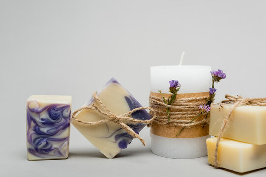 Handmade soap near candle with flowers on grey background.