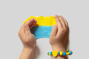 A child make the flag of Ukraine dough. Child with plasticine in the colors of the flag of Ukraine in hands. Children's creativity. DIY holiday handicraft and craft tools. Pray for Ukraine.