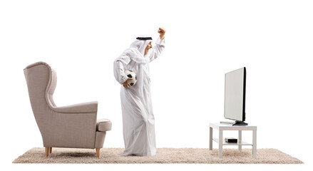 Full length profile shot of an arab holding a football and cheering in front of tv