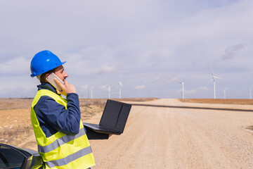 Maintenance operator at a wind farm talking to his work team on his mobile phone. Young adult man in engineering internship in renewable energy installations.