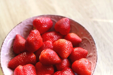 Pink bowl full of fresh strawberries on wooden table. Selective focus.