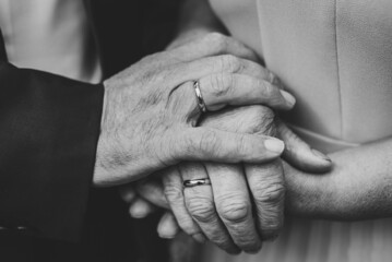 Senior woman and man hold hands with each other, retirement life. Elderly community concept, closeup. Elderly couple together outdoors. Focus on hands. Close up. Black and white photo.