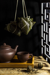 Rice dumpling zongzi hanging over a tea set - Traditional sweet Chinese food for Dragon Boat Duanwu Festival celebration in rustic tone