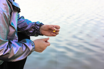 A fisherman threads bait on a hook of a fishing rod going to catch fish. Woman's hands on backdrop of smooth calm water in lake, river with room for text. Hunting concept. Angler skewer fish feeder.