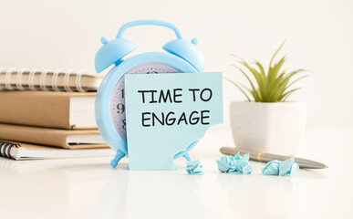 On a delicate pink background, blue alarm clock and a wooden frame with the text TIME TO ENGAGE