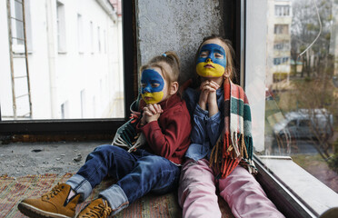 Fototapeta na wymiar Two little girls with Ukrainian flags painted on their faces are praying for Ukraine, a gesture of faith and hope. Children are against war