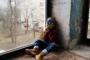 a little Ukrainian patriot girl with the flag of Ukraine on her face prays sitting at the window....