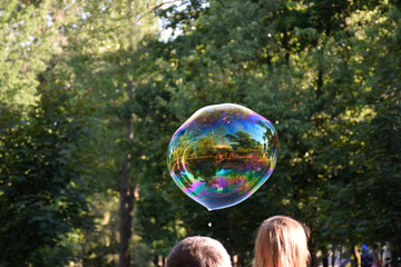 Soap bubble over the heads of a girl and a guy. Rainbow bubble on green foliage background