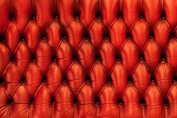 Frontal view of vintage red leather sofa or couch with visible buttons, stitches and soft upholstery. Steampunk style furniture.