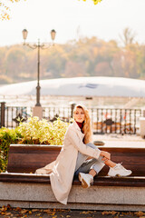 a beautiful blonde in a coat and jeans on the bench in an autumn park. 