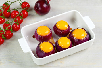 Stuffed onions recipe. Red onions stuffed with meat and vegetables inside and eggs on top in white bowl ready to bake in the oven. close up