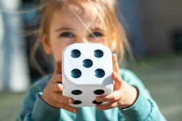Child with a large white dice with the number 5 on the street during the day