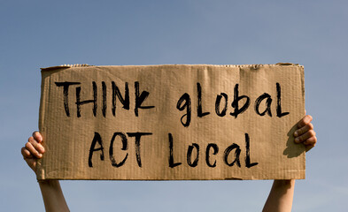 A poster with the words THINK GLOBAL, ACT LOCAL in the hands of a young girl against a blue sky.