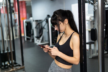 Fototapeta na wymiar Caucasian young woman using smartphone in the gym while taking a break