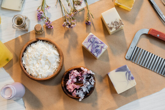 Top view of soap flakes near flowers and bars on craft paper on table.