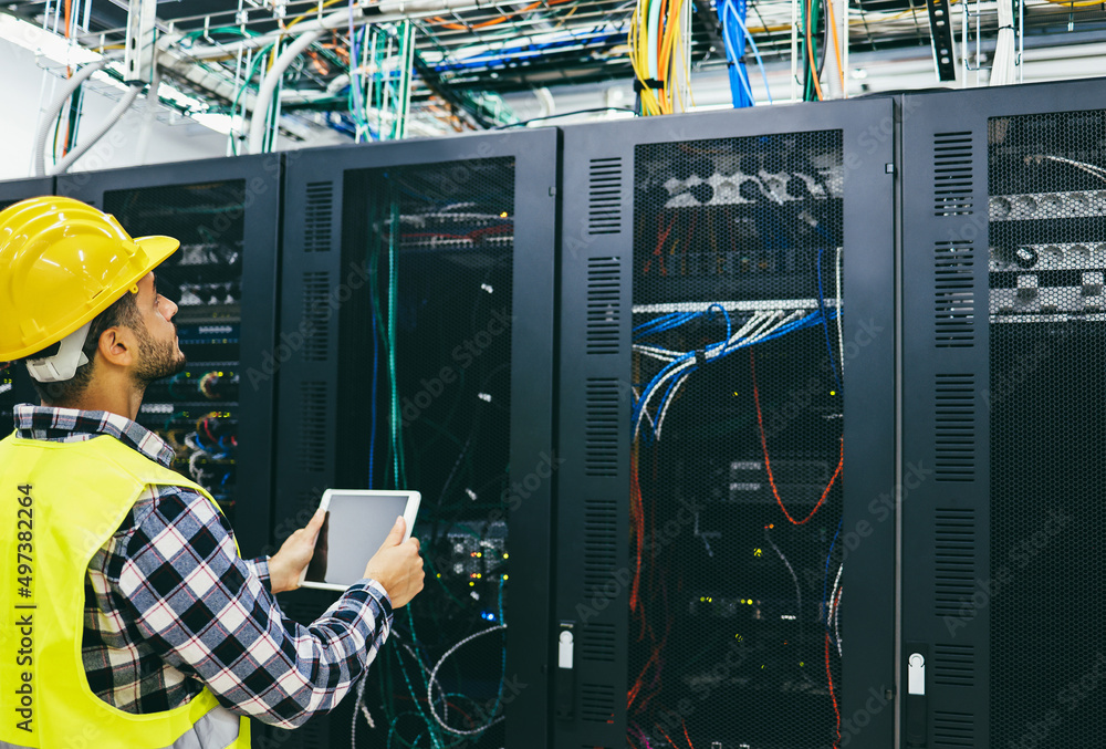 Wall mural Young technician man working with tablet inside big data center room - Focus on face