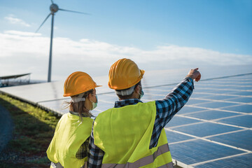 Fototapeta premium People working for solar panels and wind turbines at renewable energy farm wearing safety masks - Focus on woman helmet