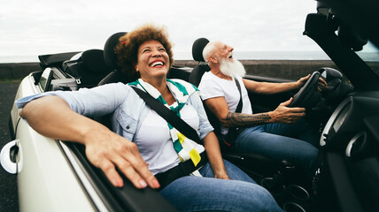 Happy senior couple having fun in convertible car during summer vacation - Focus on woman face - obrazy, fototapety, plakaty