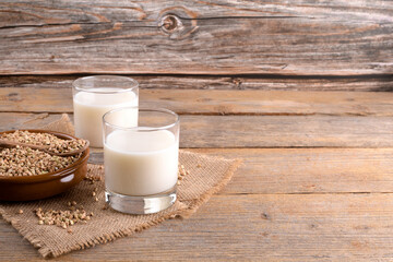 Vegan non diary buckwheat milk in glasses with buckwheat groats in a clay bowl on a wooden background. Vegan buckwheat drink is plant based alternative milk . Veggies healthy milk product, copy space