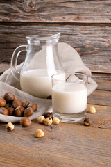 Vegan non diary hazelnut milk in glass and jug with whole hazelnuts on a linen napkin on a rustic wooden background. Lactose free hazelnut drink is plant based alternative milk. Healthy milk product