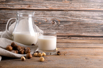 Vegan non diary hazelnut milk in glass and jug with whole hazelnuts on a linen napkin on a rustic...