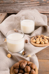 Vegan non diary hazelnut milk in glass with whole hazelnuts on a linen napkin on a rustic wooden background. Lactose free hazelnut drink is plant based alternative milk. Healthy milk product, close up