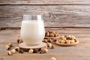 Vegan non diary hazelnut milk in glass with whole hazelnuts on a linen napkin on a rustic wooden...