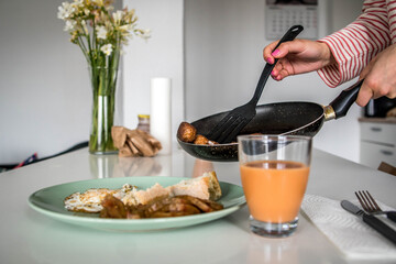 Vegan Meatballs Being Served from the Pan by Women's Hands on a Plate with Bread, Tomato Slices and a Glass of Creamed Salmorejo