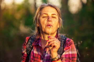 A portrait of a serious woman in her 50s who blows a dandelion to blow off his seeds.