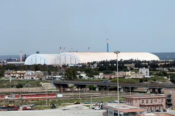 Fototapeta na wymiar Acciaierie d'Italia (English: Steelworks of Italy), formerly ArcelorMittal, Ilva and Italsider. Long cover structure required for the environmental containment of the Mineral Park. Taranto, Puglia
