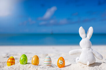 Easter travel concept with a bunny and colorful eggs sitting in the sand on a tropical paradise...