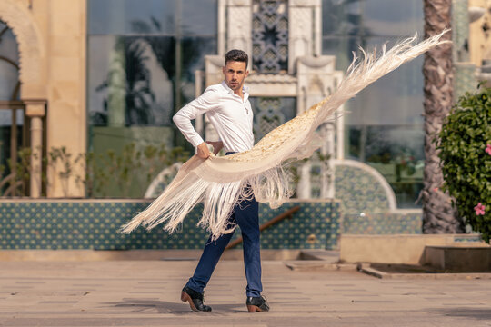 spanish flamenco dancer dressed in blue and white moving a manton around his body