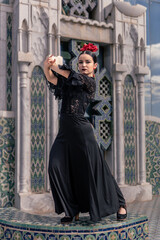 spanish young flamenco dancer dressed in black with a red rose in her hair poses on a tiled platform with Arabic decoration